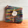 Set of two variegated rainbow crocheted potholders on a cedar bath board, tied with a piece of twine with a simple brand label.