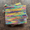 Set of two variegated rainbow crocheted potholders sitting on top of each other with a dark piece of wood as the backdrop.