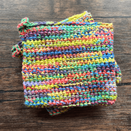 Set of two variegated rainbow crocheted potholders sitting on top of each other with a dark piece of wood as the backdrop.
