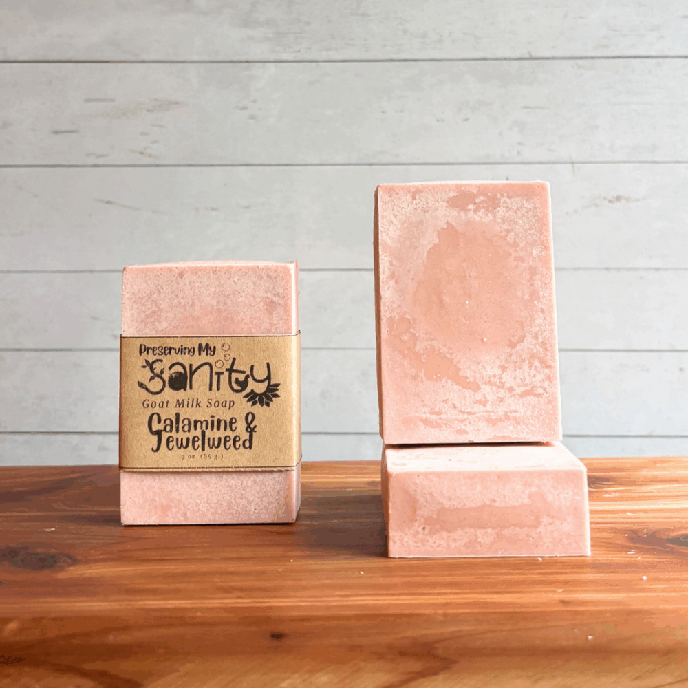 Display photo of three bars of Calamine & Jewelweed goat milk soap. The soap is light pink in color, with one bar having a label and the other two unlabeled to show detail.