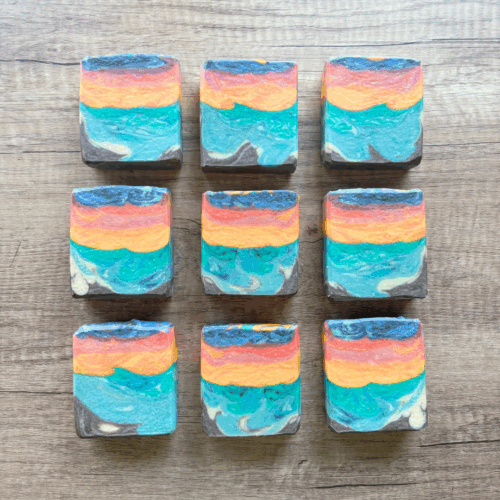 Flatlay photo showing nine bars of Candy Sunset goat milk soap, in rows of three to show the varying designs of this pretty 16-color soap that was made for the April Soap Challenge Club. Scented with a bright and fresh beachy scent, this colorful goat milk soap is a limited edition creation.