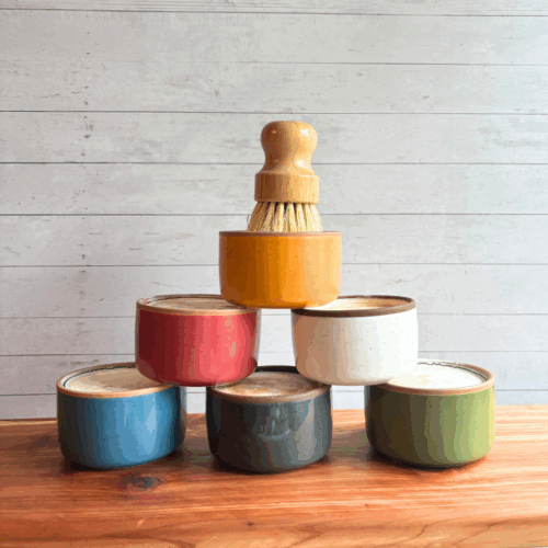 Display photo showcasing six ceramic ramekins of dish soap bars in various colors, with a bamboo dish brush sitting on top of the pyramid style display.
