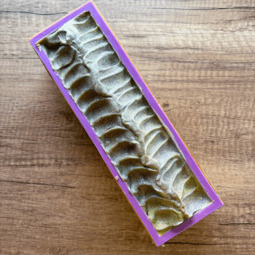One loaf of Garden Whimsy soap shown in the mold just before cutting into bars. You can see hints of green and purple in the textured top, which also has biodegradable glitter sprinkled on it.