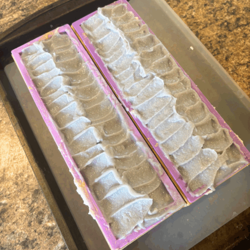 Two loaves of freshly poured Fresh Lilac goat milk soap in the molds, with a pretty textured lavender top. Made in small batches in my Minnesota kitchen.