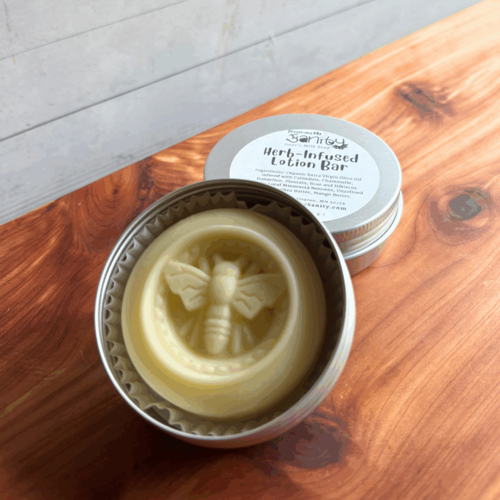 An herb-infused lotion bar with a bee pattern on top, sitting in its reusable alumnium tin with the label in the background. Sitting on a cedar board with a white paneled background.