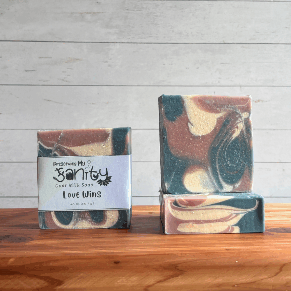 Three colorful rainbow bars of Swirl Power goat milk soap, featuring the blue, white, and pink colors of the Transgender flag in a unique swirl pattern perfect for celebrating Pride Month. The left bar is labeled, while the other two are unlabeled to show top and face design. All are sitting on a cedar board with a white paneled background.
