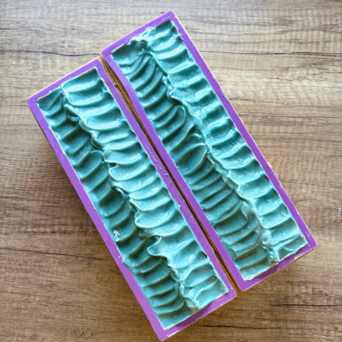 Two loaves of Shining Light goat milk soap, pictured just before cutting into bars. This soap design is modeled after the transgender pride flag, but the top is a textured pattern showing only the aqua blue color.