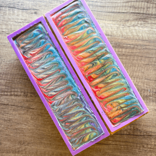Two laoves of Still We Rise goat milk soap pictured just before cutting. The tops feature a colorful swirl pattern that's perfect for celebrating Pride Month.