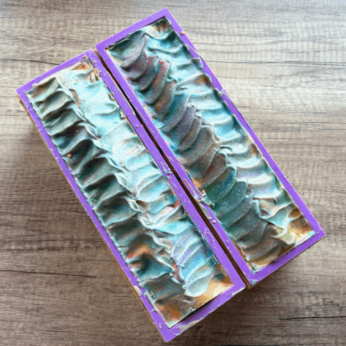 Two loaves of Swirl Power goat milk soap shown just before cutting into loaves. A plain wood background is underneath the loaves of this artisan Pride-themed soap.