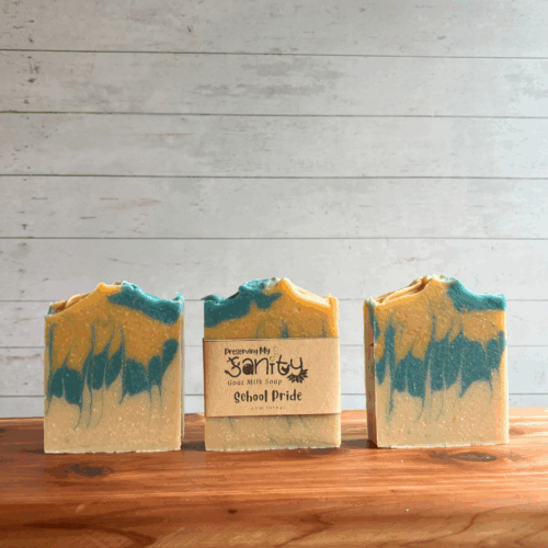 Display photo showing three bars of blue and gold School Pride soap. The middle bar has a label, the other two bars are unlabeled to show soap design. All are sitting on a cedar board with a white panel background.
