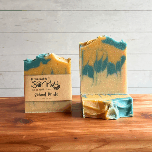 Display photo showing three bars of blue and gold School Pride soap. The left bar has a label, the other two bars are unlabeled to show top and face detail. All are sitting on a cedar board with a white panel background.