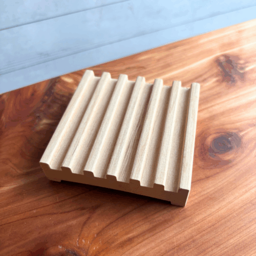 Display photo showing a square natural wood soap dish, displayed on a cedar board with a white panel background.
