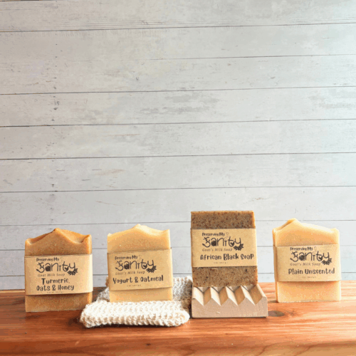 Alternative view display photo showing the contents of the Unscented Soap Sampler - half size bars of Yogurt & Oatmeal soap, African Black soap, Turmeric, Oats & Honey Soap, and Plain Unscented Soap. The sampler also comes with a natural wood soap dish and sisal soap saver bag. All of these items are displayed on a cedar board with a white panel background.