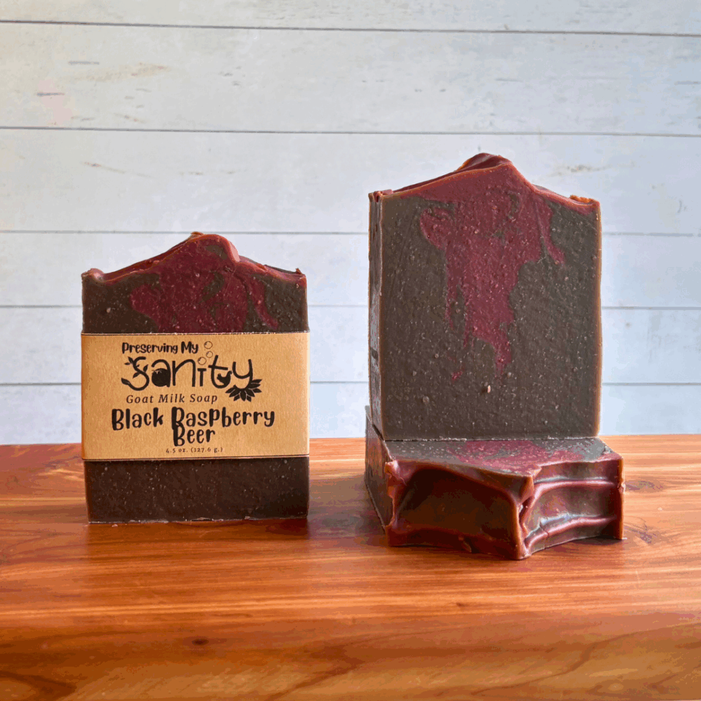 Three bars of Black Raspberry Beer goat milk soap. Soap is a dark brown color to mimic stout beer, swirled with a dark raspberry color - reminiscent of my favorite beer from a great brewery. Two bars are displayed to show the design and top of the bars, while the third shows the label.