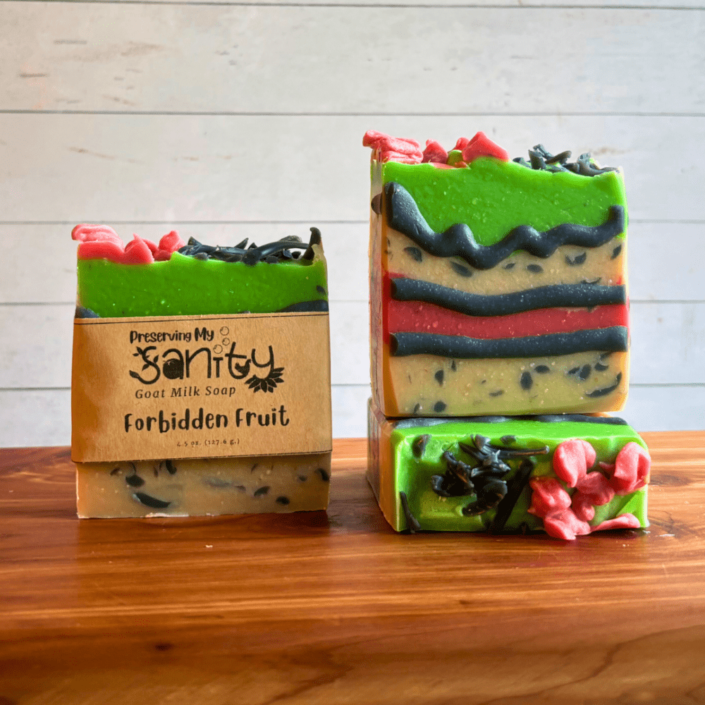 Three bars of Forbidden Fruit goat milk soap. This soap was created as part of my paranormal collection, but also for the comic cakes Soap Challenge Club contest. Soap has layers of white, red, and green and is outlined with black piping and has charcoal sprinkle embeds. Two bars are displayed to show the design and top of the bars, while the third shows the label.