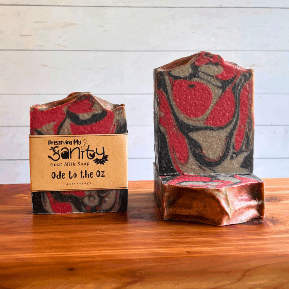 Three bars of Ode to the Oz goat milk soap. This soap is a nod to Ozzy Osbourne, made with Dragon's Blood fragrance and groovy wirls of black, silver, and red. Two bars are displayed to show the design and top of the bars, while the third shows the label.