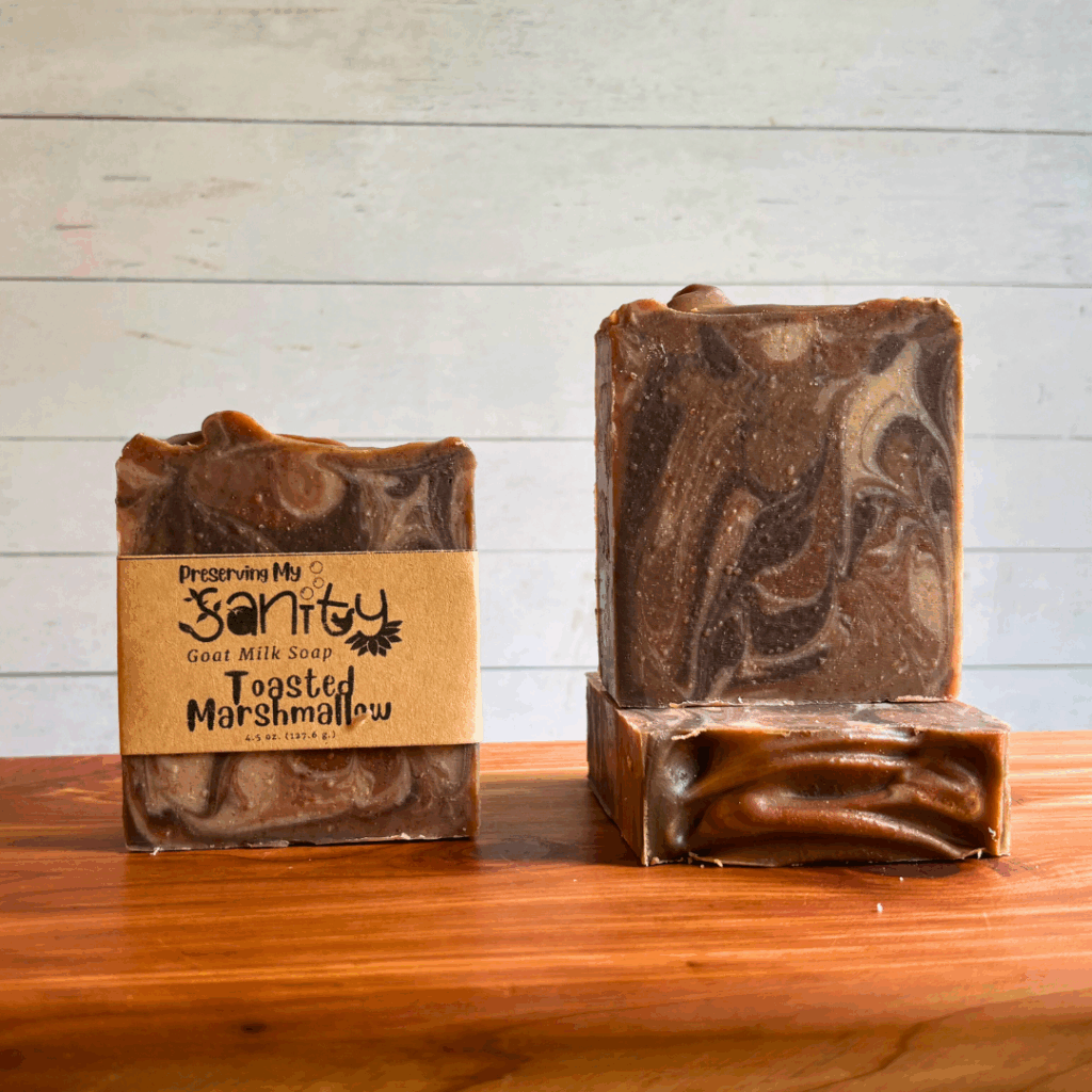 Display photo showcasing three bars of handcrafted Toasted Marshallow goat milk soap, one bar with a label and the other two without labels to show the pretty dark brown swirls in this artisan soap. The bars are lightly topped with some copper mica.