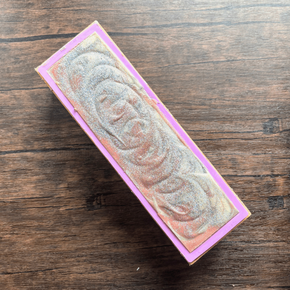 Process photo showing a full loaf of Silver Sparkle goat milk soap before cutting into bars. You can see silver sparkle glitter on the top, and below that red, sliver and white soap batter.