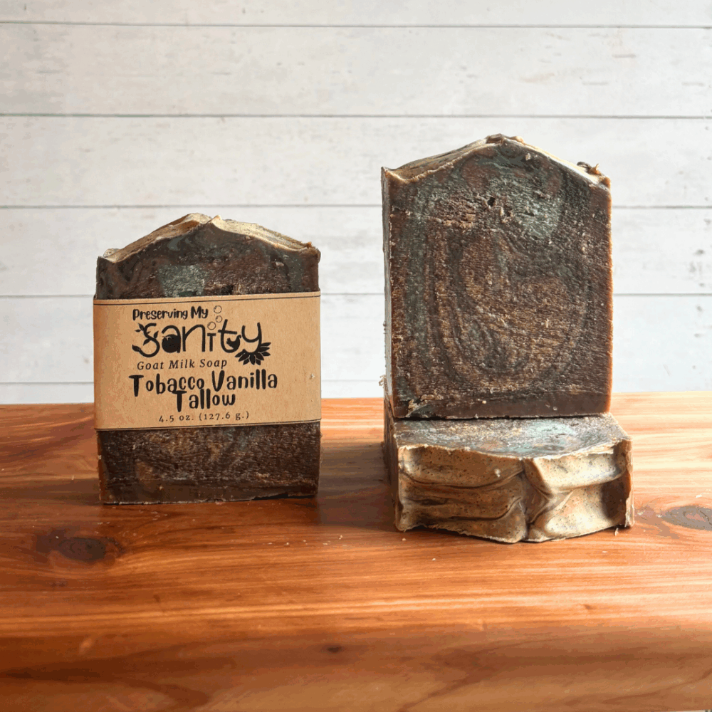 Three bars of Tobacco Vanilla tallow soap, made with locally sourced fresh goat milk. The soap is dark brown with light brown and light blue swirls. It has a rustic look to it, and the top was textured with the back of a spoon.