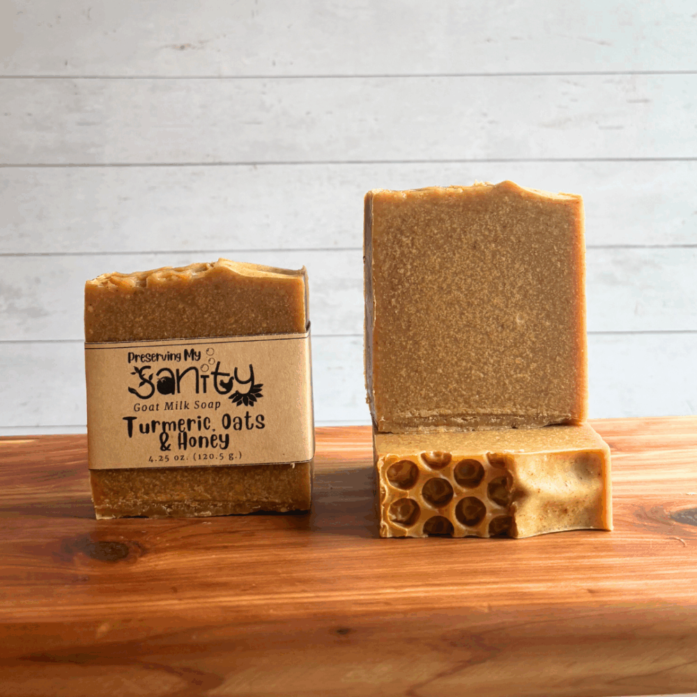 Display photo showing three bars of Turmeric, Oats & Honey goat milk soap with a honeycomb textured top. Bars are pictured to show different angles of the soap, with one bar having a label on it. Soap bars are sitting on a cedar bath board.