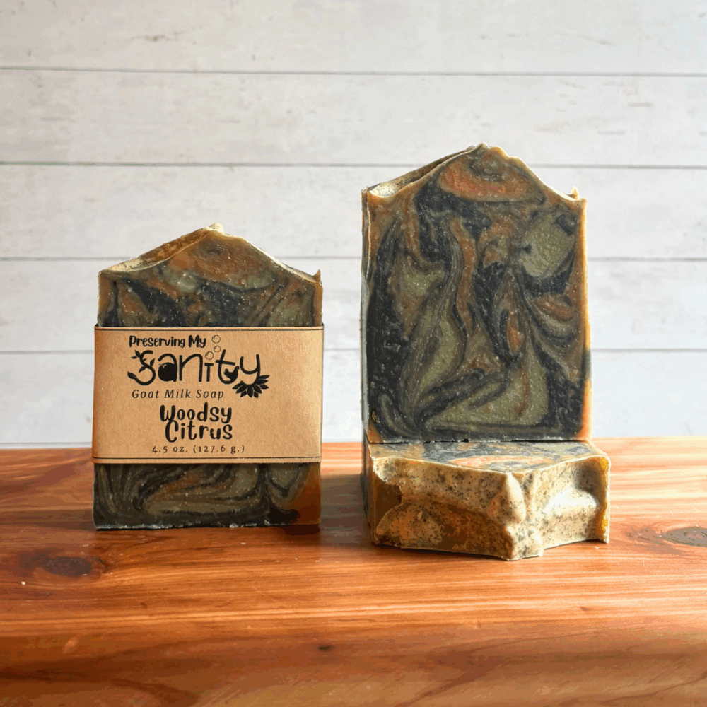 Three bars of Woodsy Citrus goat milk soap, made with plant-based colorants and an essential oil blend of rosemary, orange, and cedarwood. The colors were swirled together and just look really pretty like a swirled walk in the woods. Two bars are pictured without the label, and one with - and displayed to show different angles of the soap.
