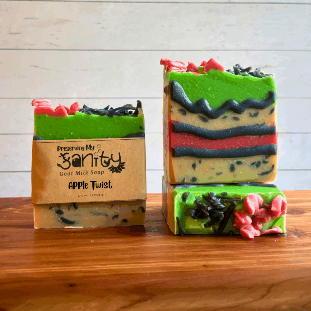 Three bars of Apple Twist goat milk soap. This soap was created as part of my paranormal collection, but also for the comic cakes Soap Challenge Club contest. Soap has layers of white, red, and green and is outlined with black piping and has charcoal sprinkle embeds. Two bars are displayed to show the design and top of the bars, while the third shows the label.
