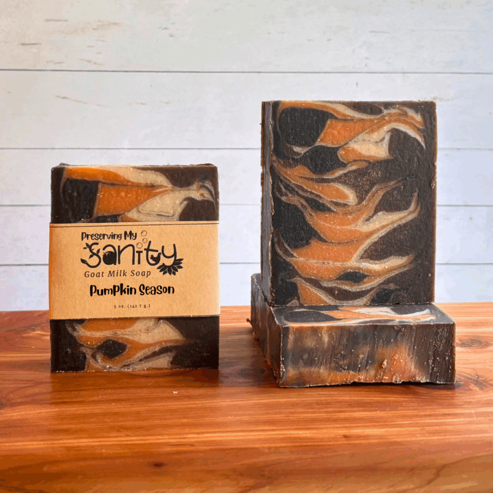 Three bars of Pumpkin Season goat milk soap. The soap is a Taiwan swirl design of black, brown, orange, and white. Two bars are displayed to show the design and top of the bars, while the third is laid flat on the board to display the soap top.