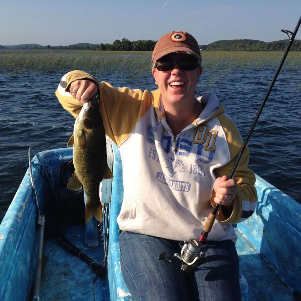 Darcy holding a largemouth bass while fishing on a lake from a small blue boat.