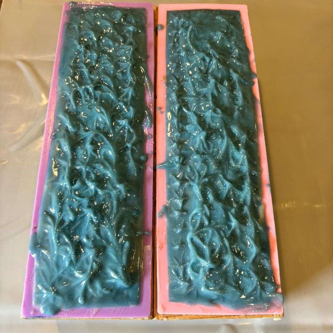 Two freshly poured Day at the Beach soap loaves rest in purple and pink silicone molds during the soapmaking process. The tops feature textured peaks and swirls in rich ocean blue, creating a wave-like pattern that reflects the soap's coastal inspiration. The handcrafted loaves are shown before being cut into individual bars.